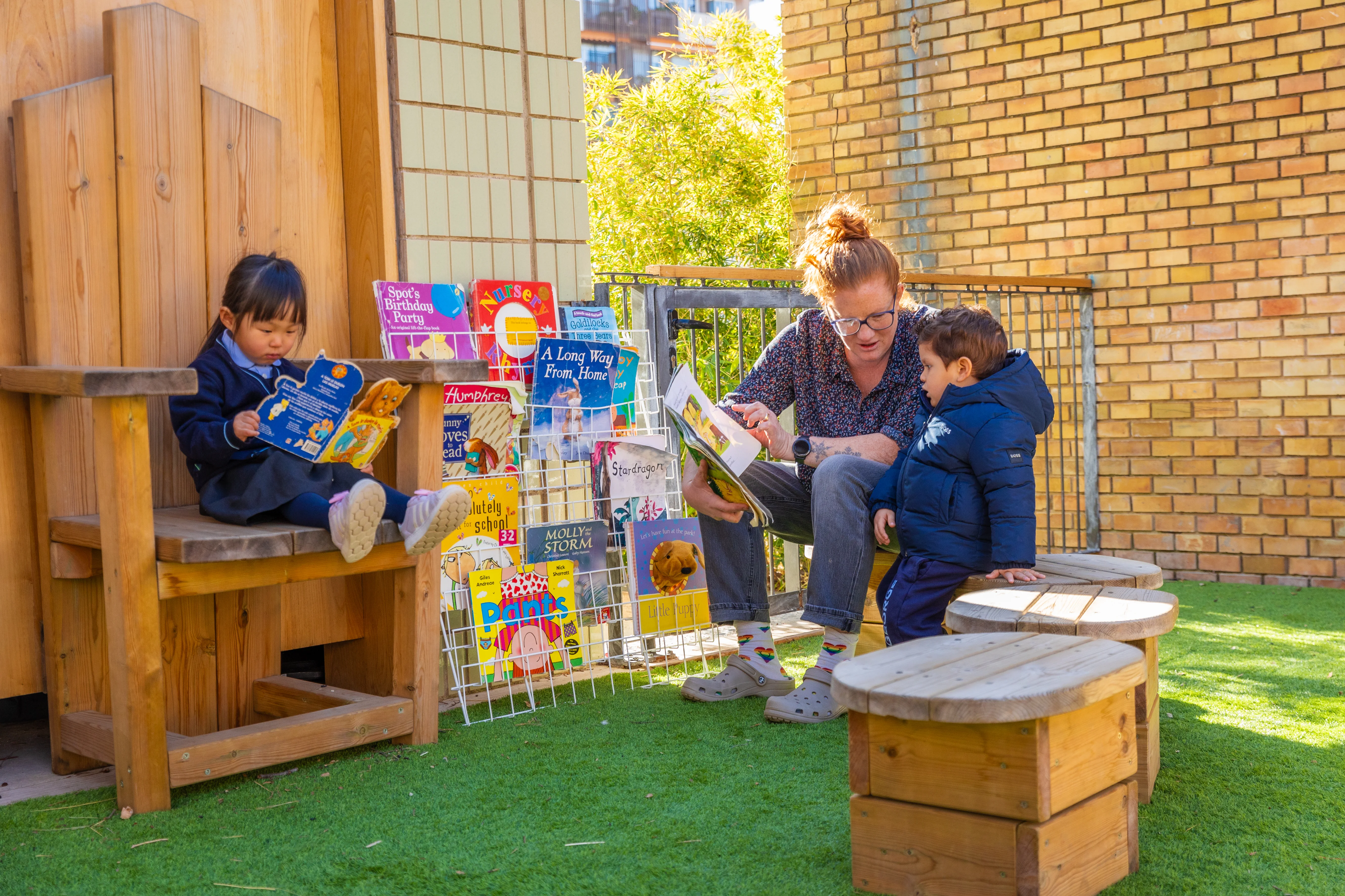 Teacher reading a book to a little student in the schoolyard and little girl reading a book 