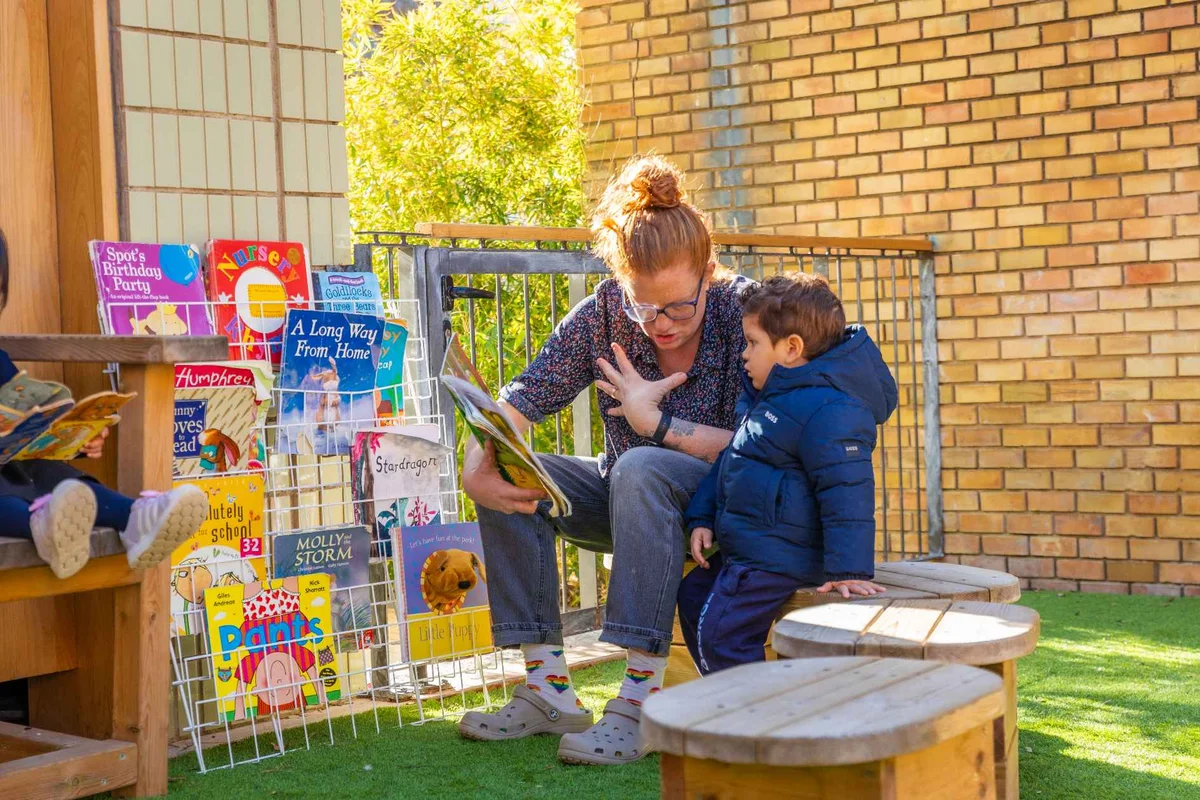 Teacher in the schoolyard reading a book to a little student